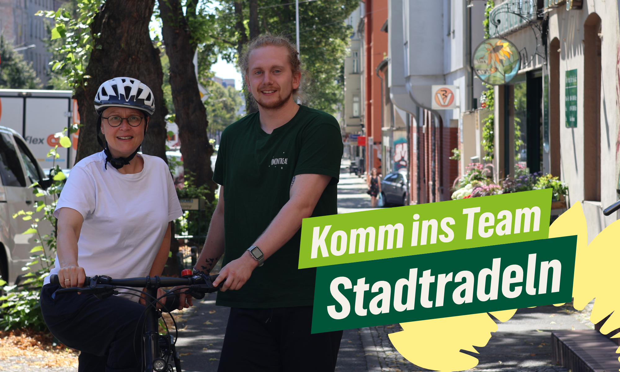 Zwei Personen, Nicole Walldorf und Jascha Rihm, stehen lächelnd mit Fahrrädern auf einer baumgesäumten Straße in einer deutschen Innenstadt. Links eine Frau mit weißem Fahrradhelm, Brille und weißem T-Shirt, rechts ein junger Mann mit längeren Haaren in einem grünen T-Shirt mit der Aufschrift "MONTREAL". Beide halten ihre Fahrräder fest. Im Vordergrund ist ein auffälliges grün-gelbes Werbebanner mit dem Text "Komm ins Team Stadtradeln" zu sehen. Im Hintergrund sind typische deutsche Stadtarchitektur mit Geschäften, Bäumen und parkenden Autos erkennbar. Die Szene vermittelt eine freundliche, umweltbewusste Atmosphäre und bewirbt offensichtlich das Stadtradeln-Programm, eine Initiative zur Förderung des Fahrradfahrens in deutschen Städten.