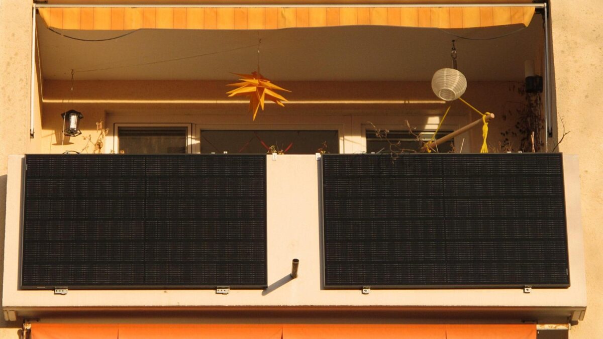 Das Bild zeigt einen belebten Balkon, vor dem zwei schwarze Solarpanele hängen.